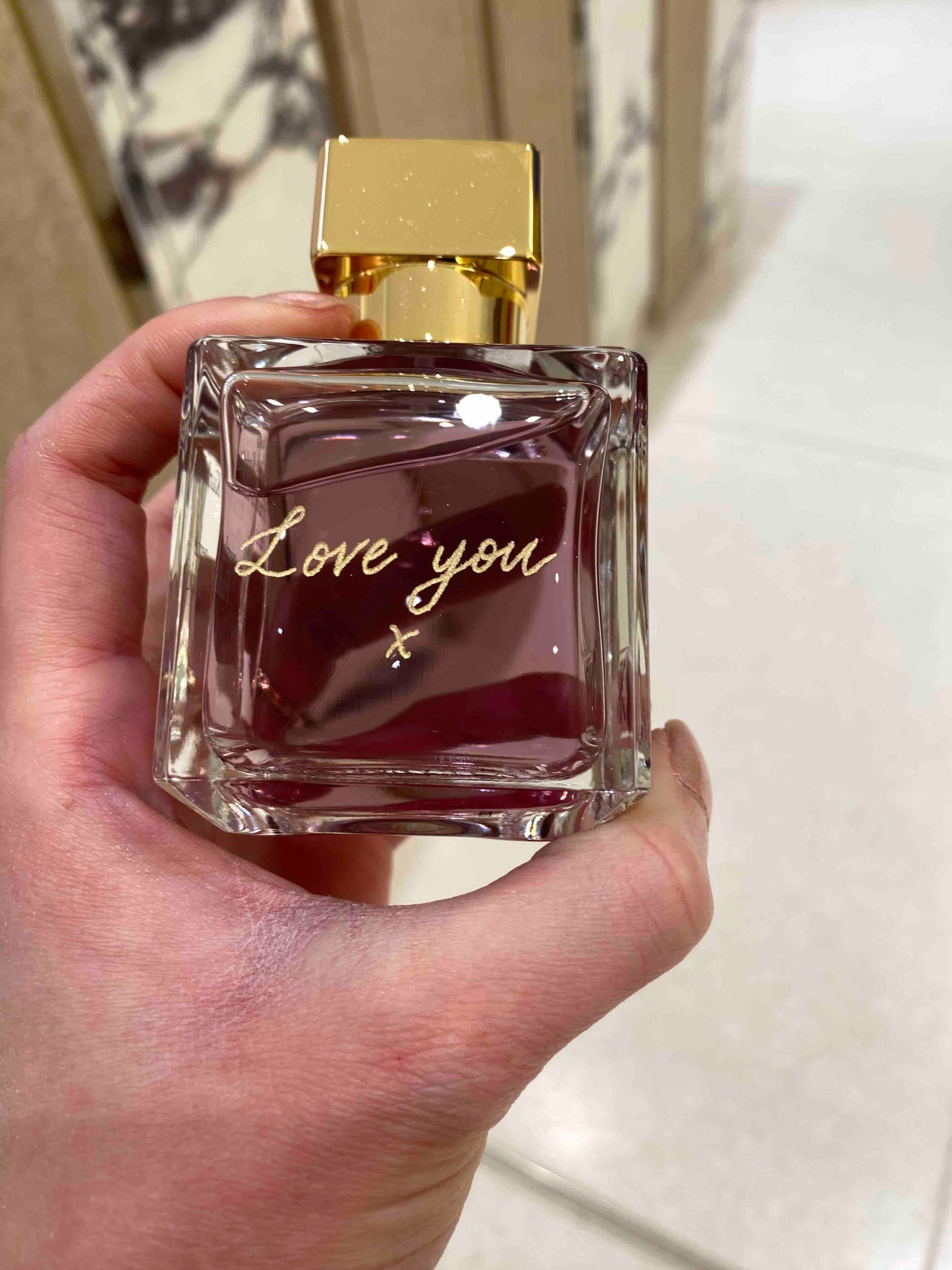 Perfume bottle with 'Love you' text held in a hand against a neutral background