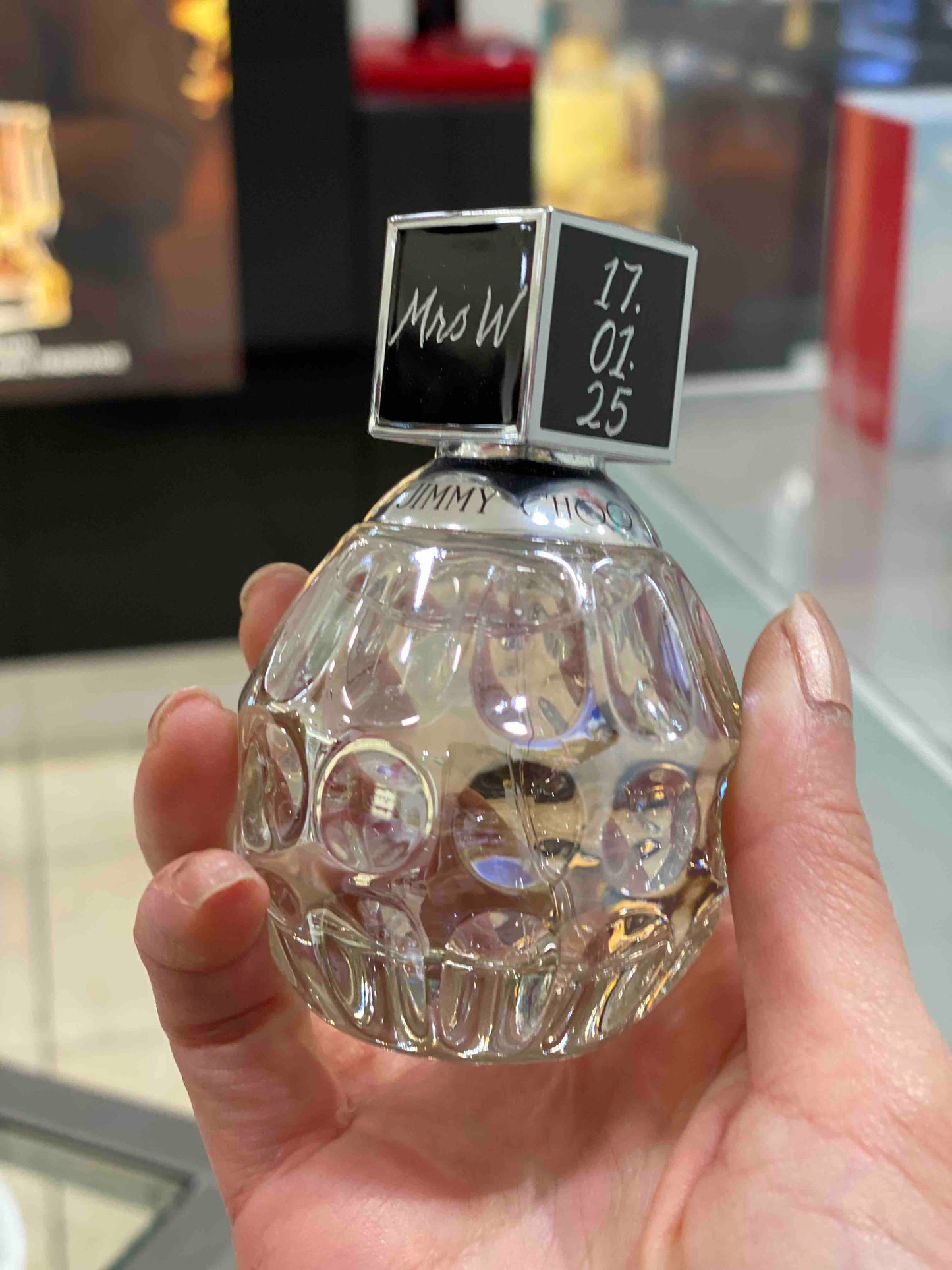 Hand holding a clear perfume bottle with a personalised cap, featuring the brand ‘Jimmy Choo'.