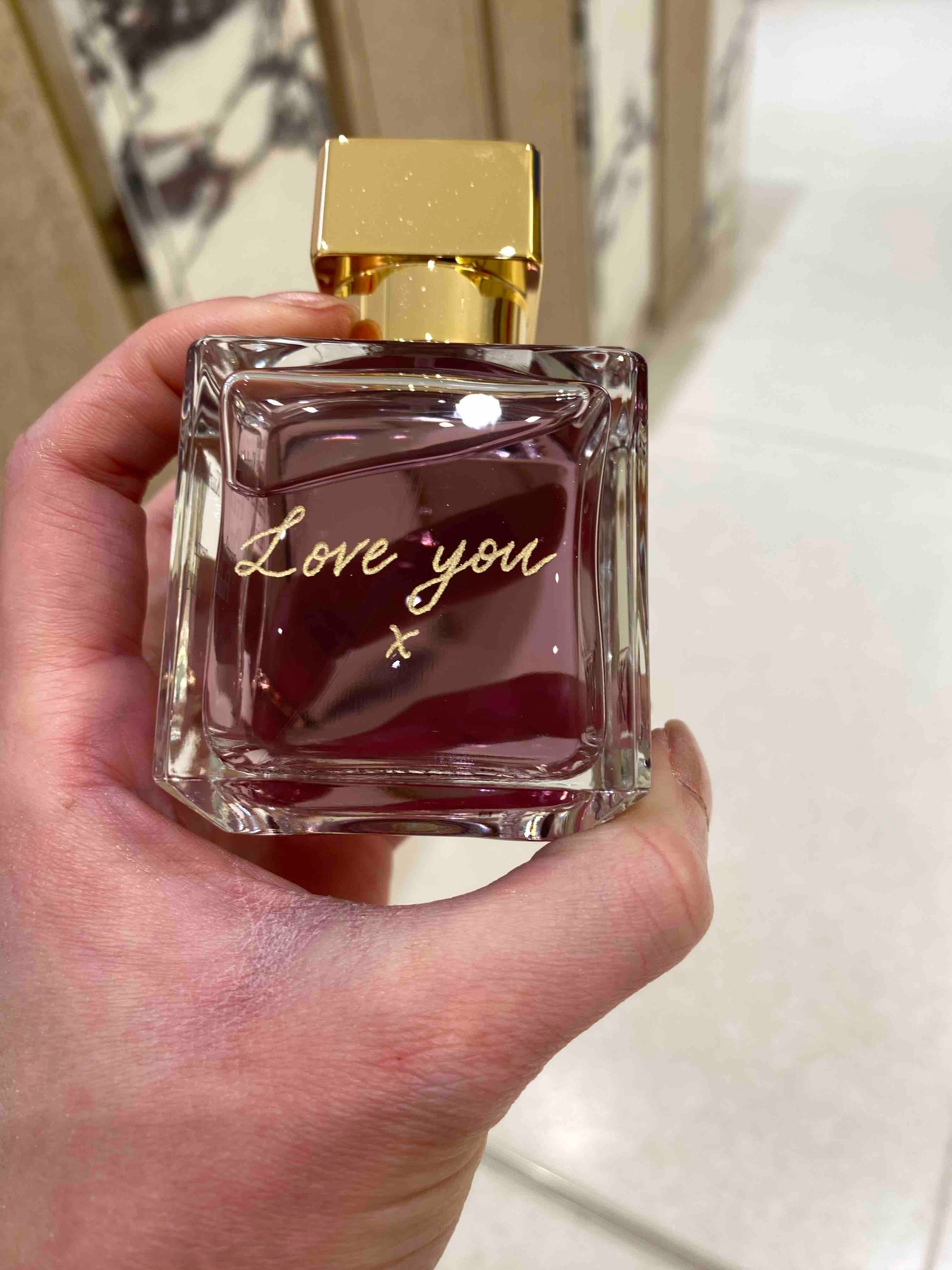 Perfume bottle with 'Love you' text held in a hand against a neutral background
