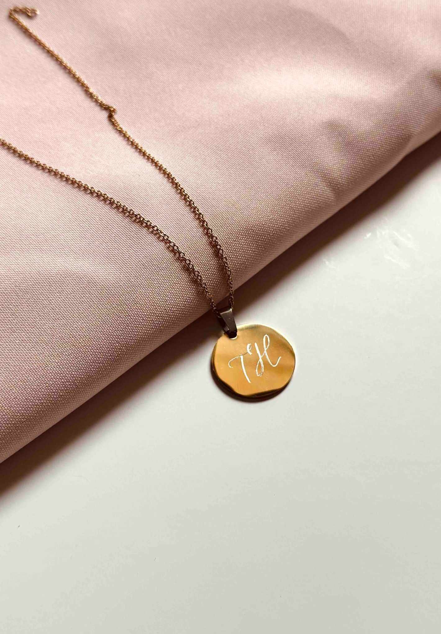 dainty gold initial necklace lying on a pink cloth and white surface